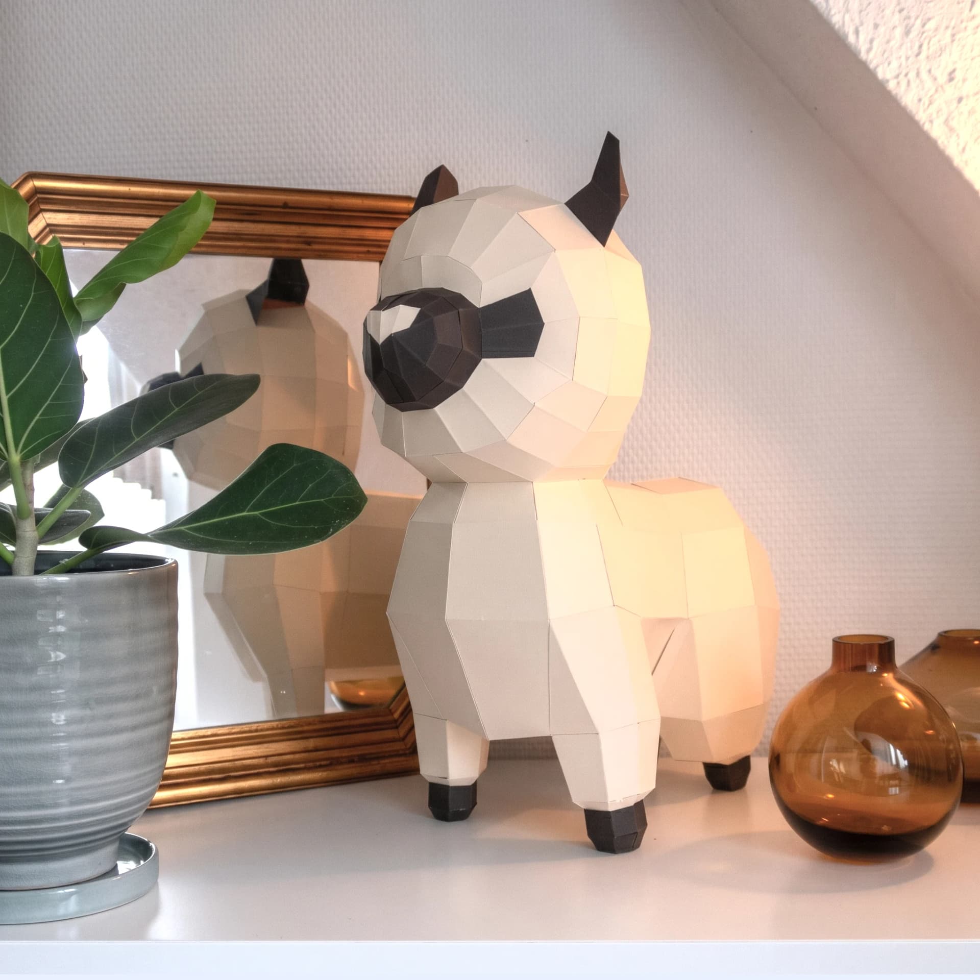 Décoration origami 3D en papier de bébé lama beige posé sur une commode à coté d'une plante