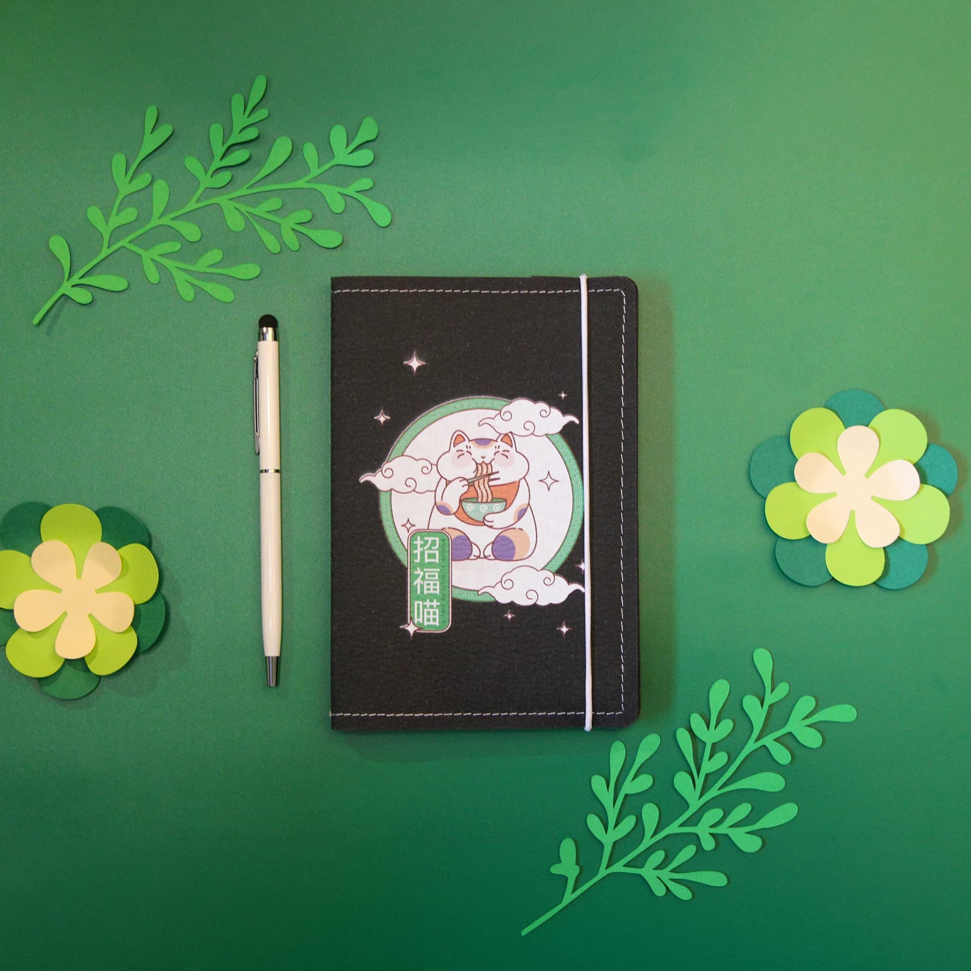 Papeterie couverture en cuir de carnet A6 avec une illustration kawaii de Maneki Neko, un stylo et des fleur en papier