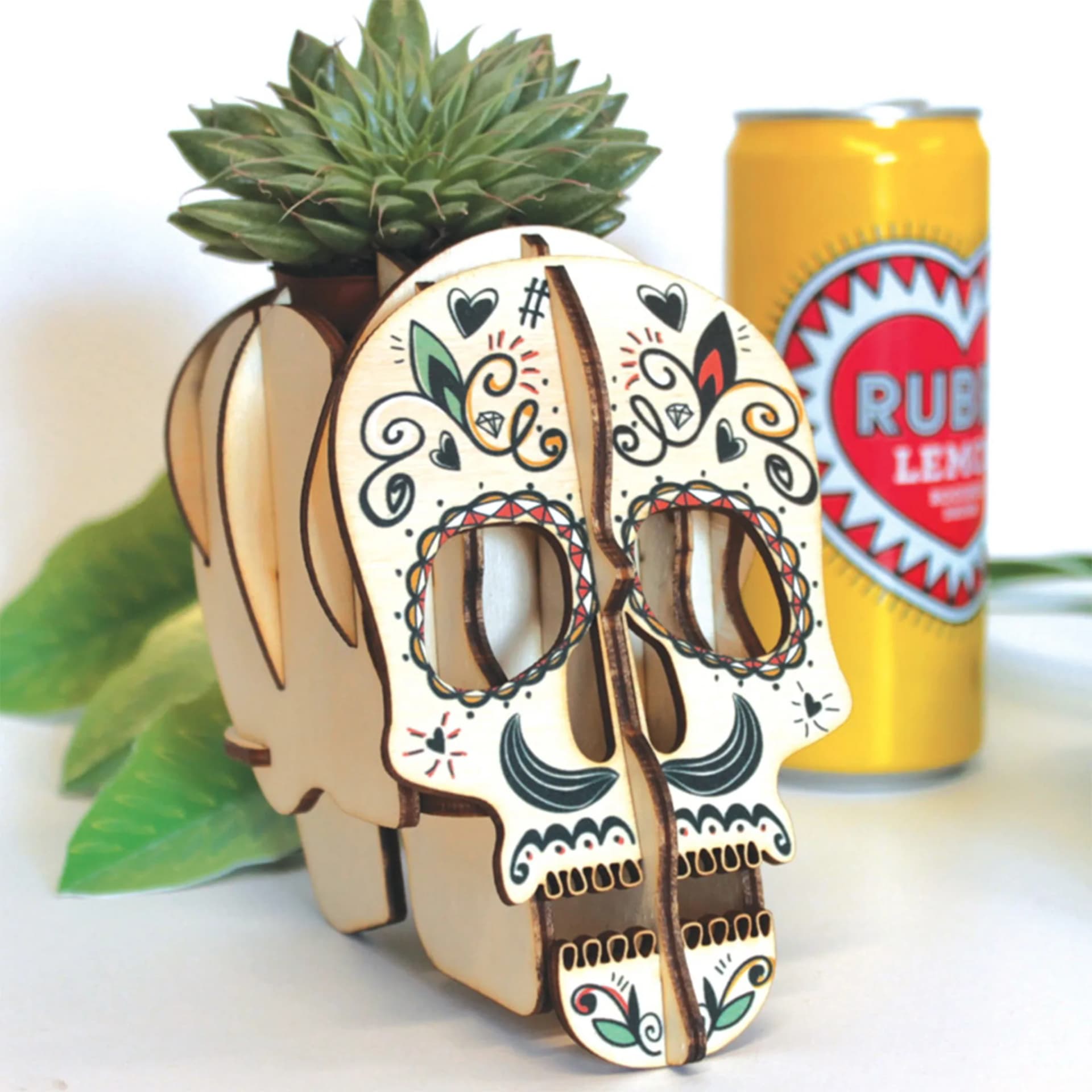 Décoration crâne calavera en bois posé devant de la végétation et une boisson