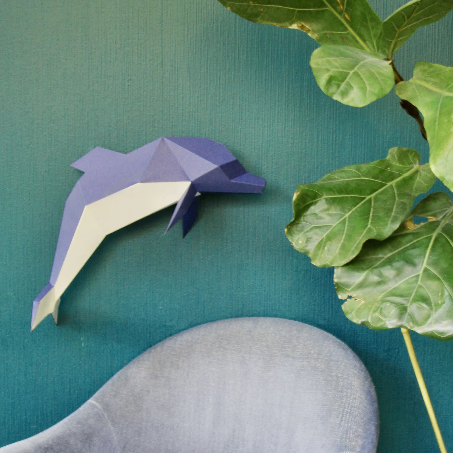 Décoration origami dauphin en papier Bleu sur un mur bleu avec des plantes