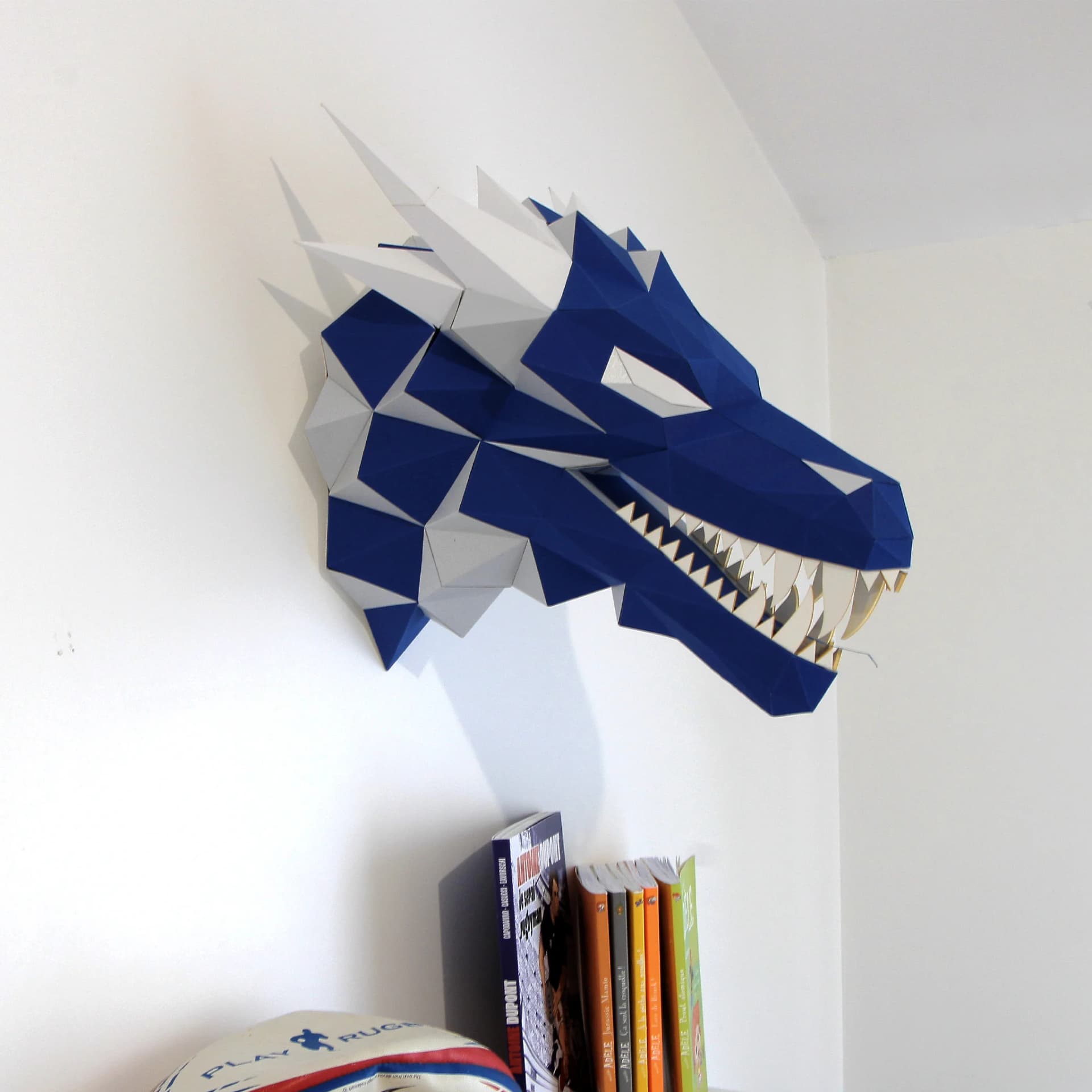 Décoration origami dragon en papier bleu & argent sur un mur au dessus de livres