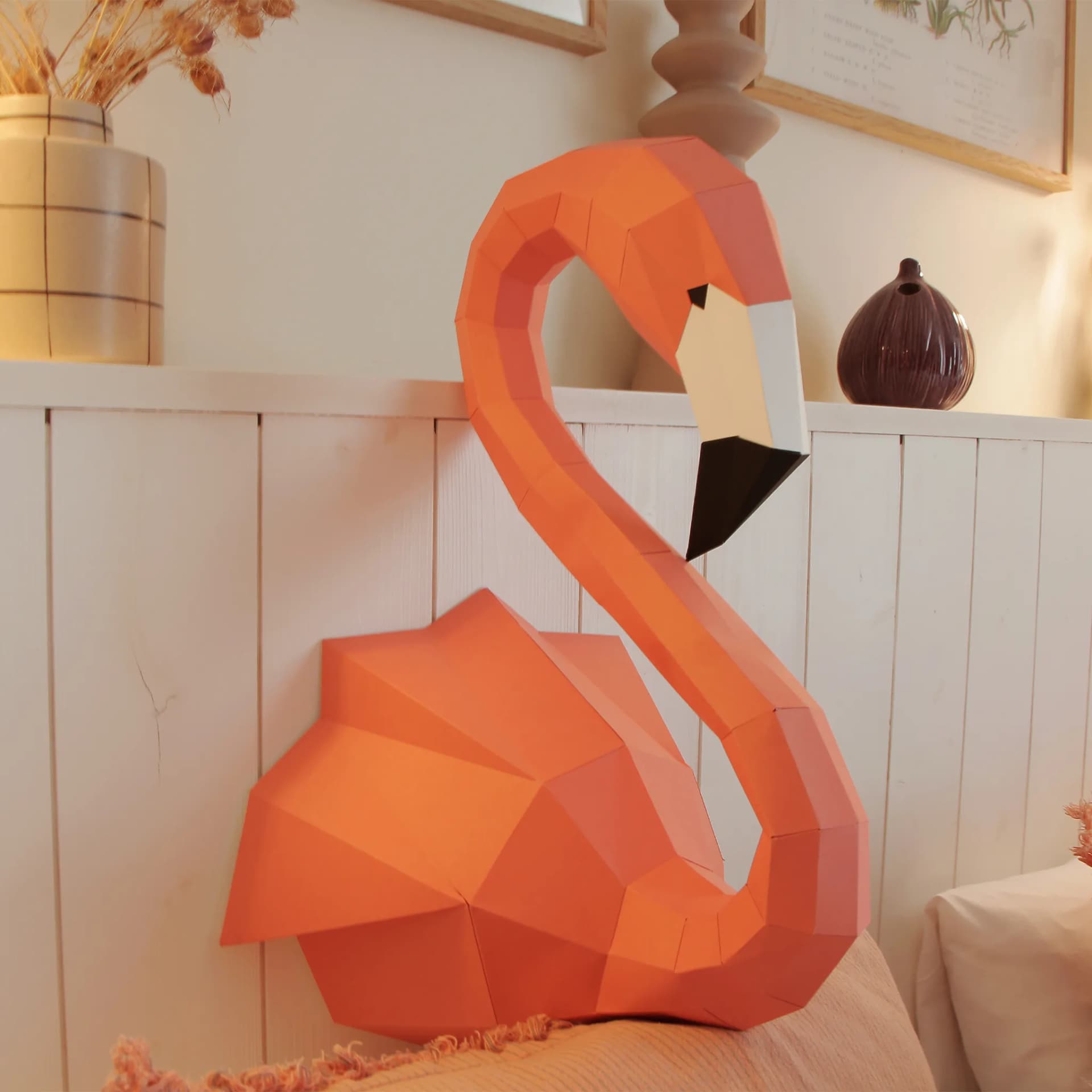 Décoration origami flamant rose en papier 3D dans un salon posé sur des coussins contre un mur