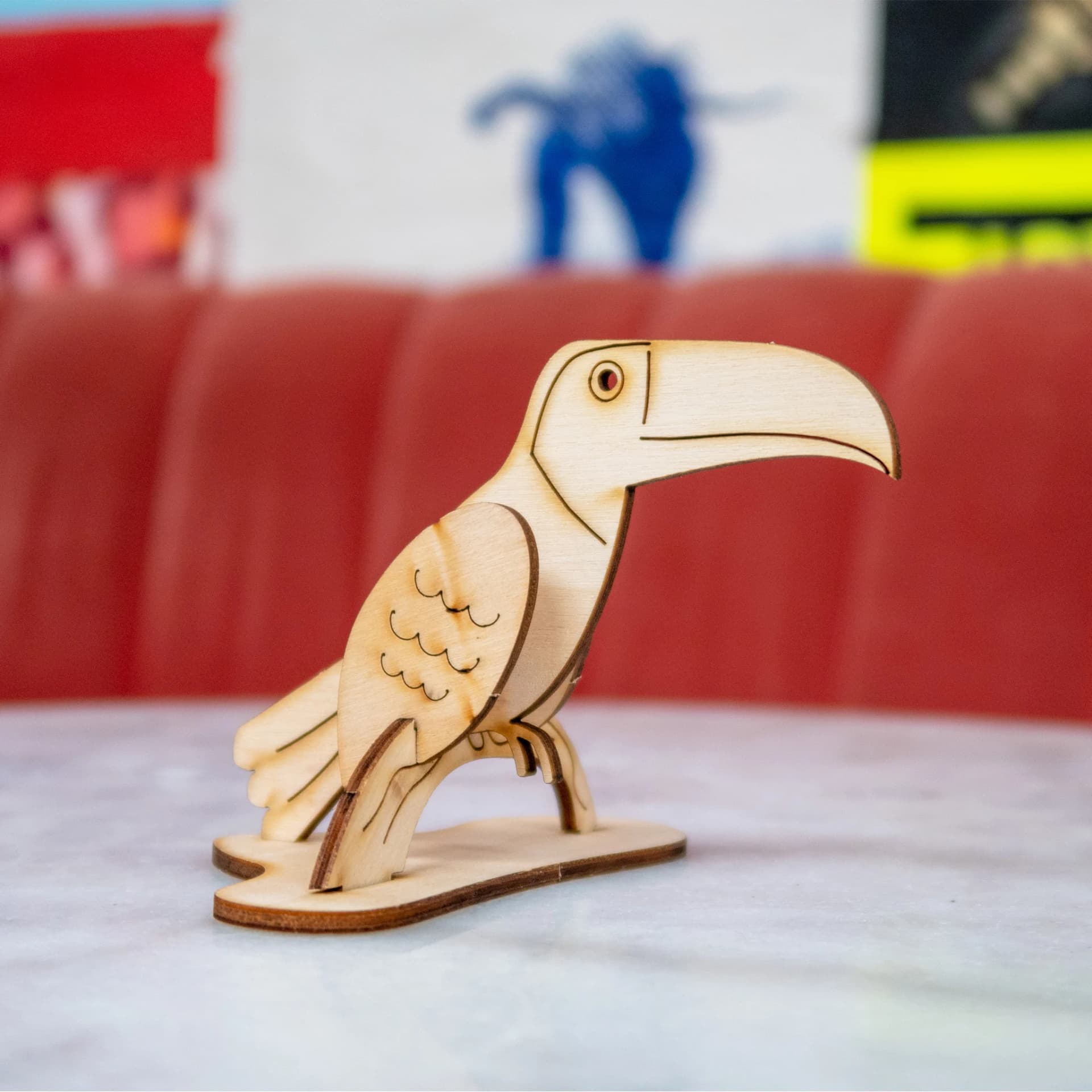 Décoration les p'tits bidules en bois Toucan posé suyr une table devant un canapé rouge et un fond coloré