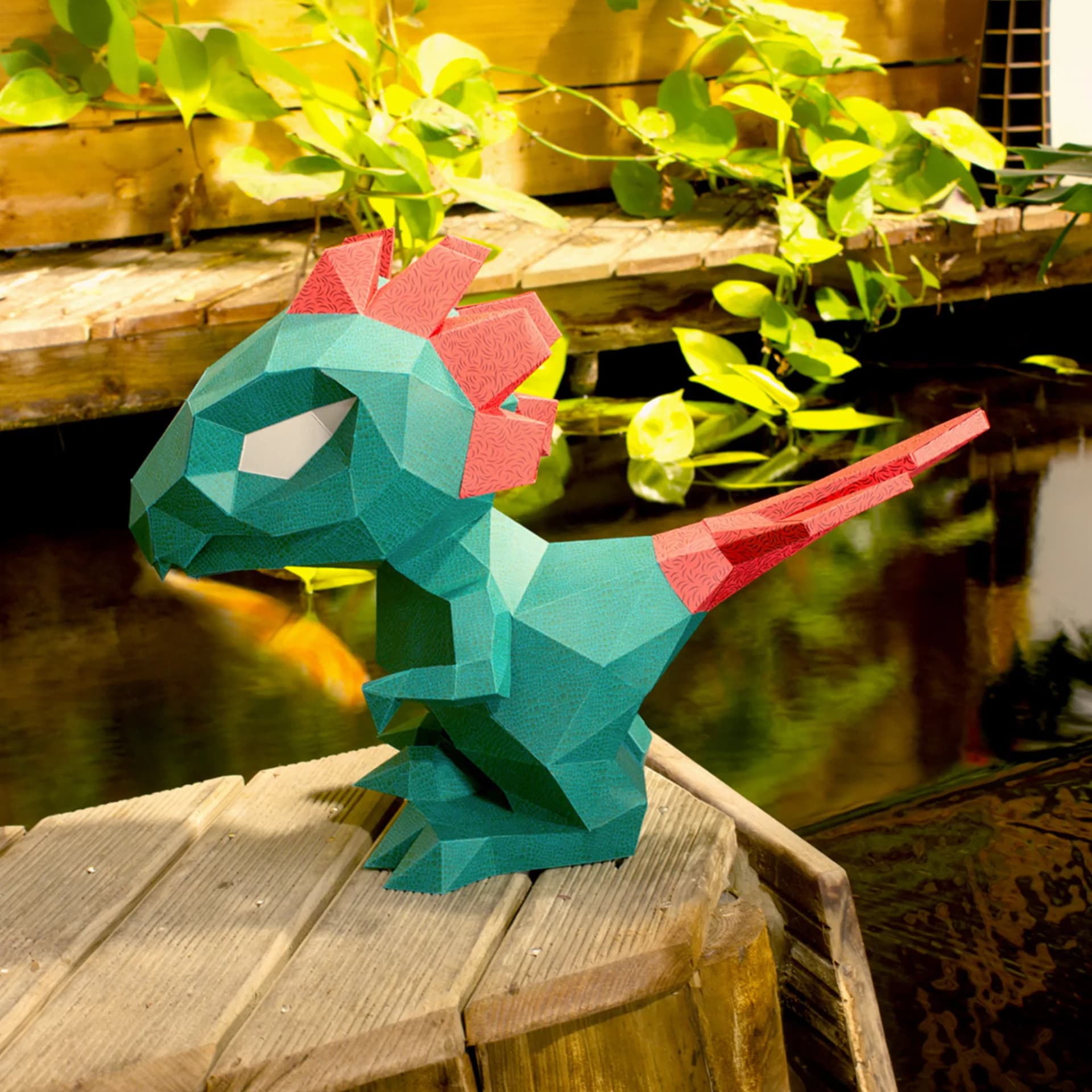Décoration origami Petit dino en papier Vert et rouge posé sur des planches en bois devant un bassin d'eau