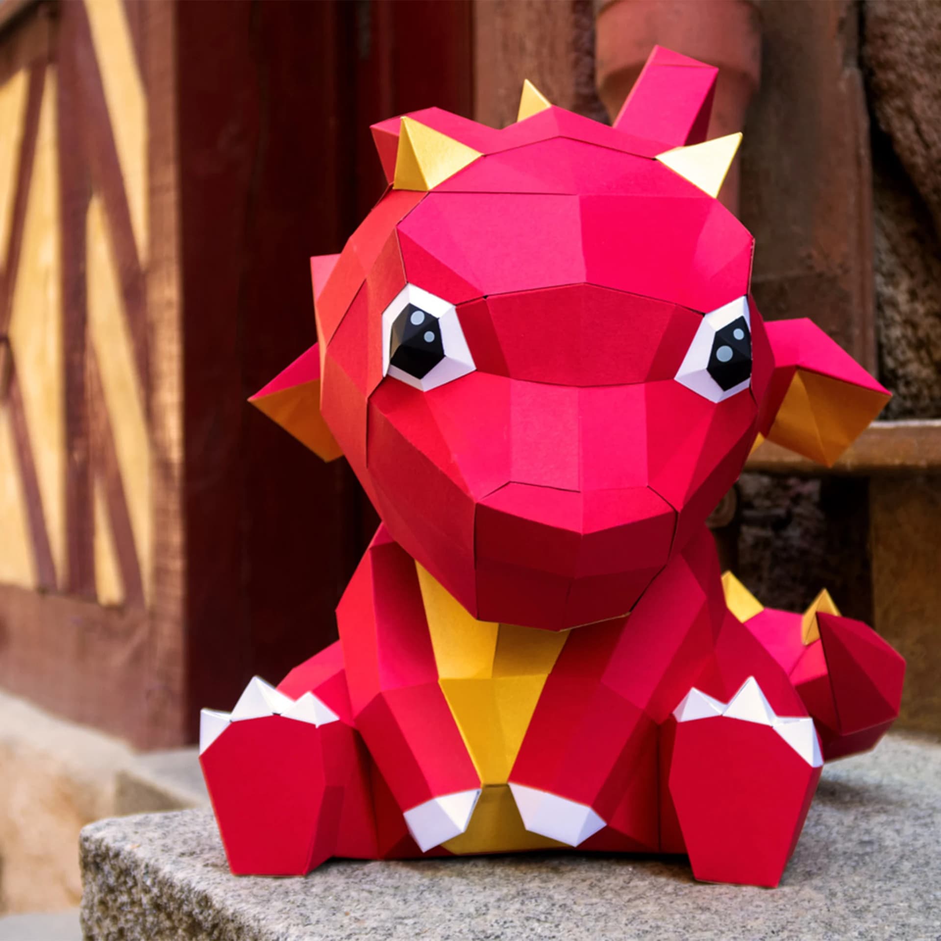 Décoration origami Petit dragon en papier posé sur une marche en pierre devant une maison en colombage