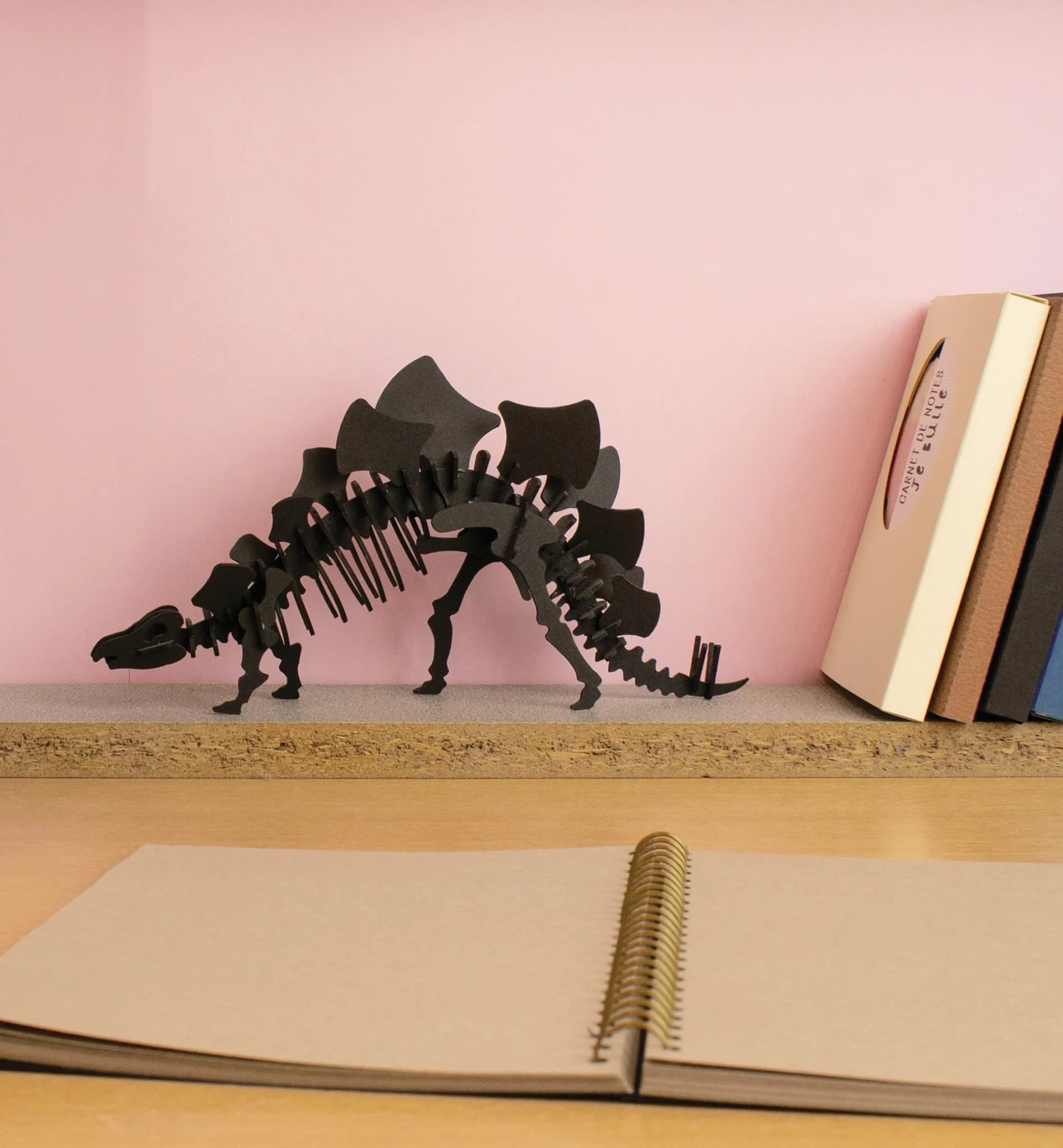 Décoration Stegosaurus en carton sur un bureau à côté de livres, devan tun mur rose