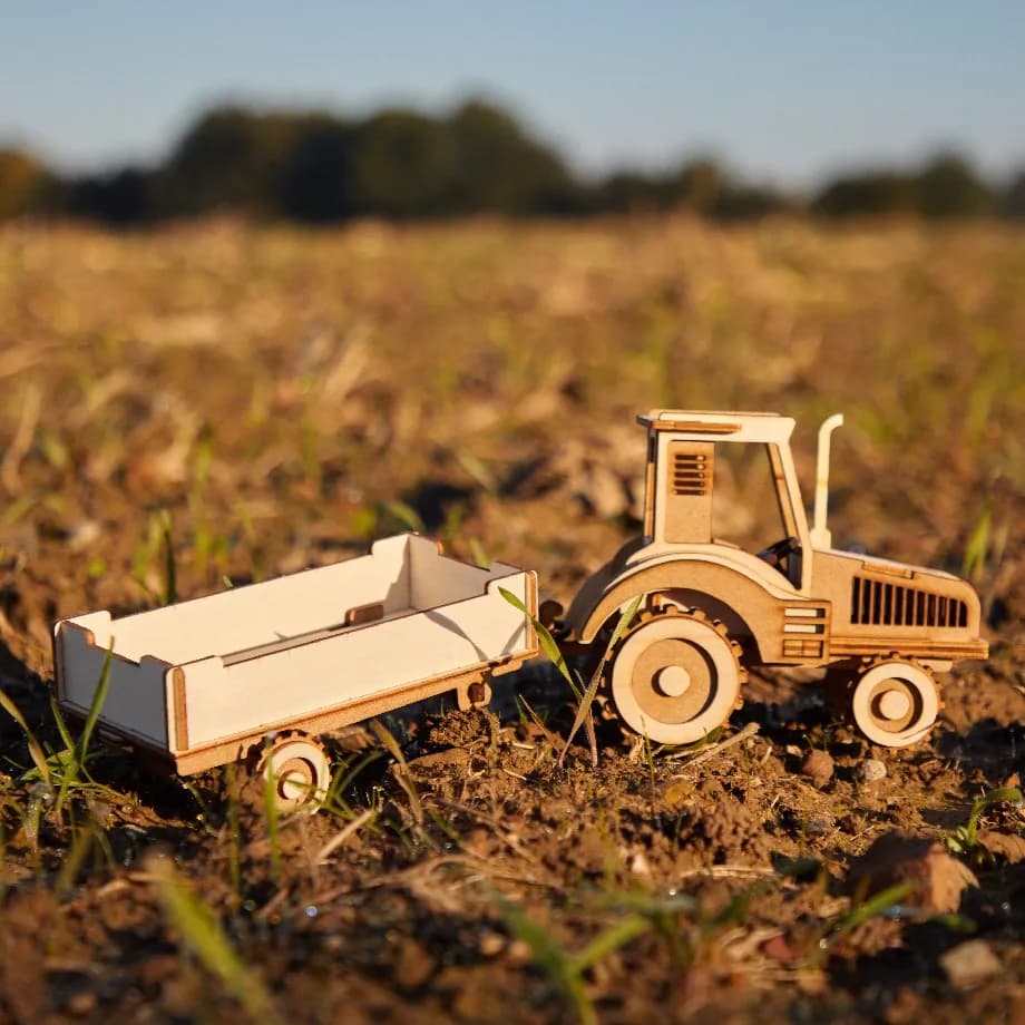Décoration en bois d'un tracteur à monter soi-même, posé dans un champs de blé, près d'une maison de campagne