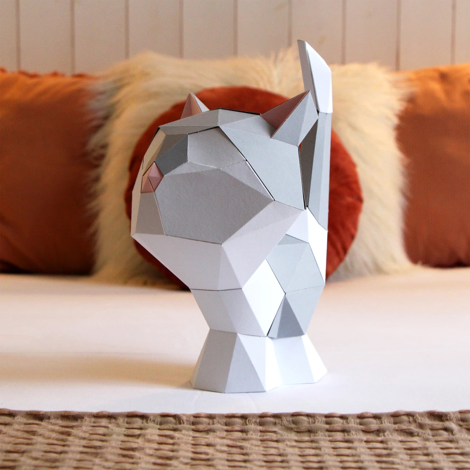 Décoration en papier trophée babies chat blanc et gris assis sur un lit dans une chambre couleur terracota, sur un plaid