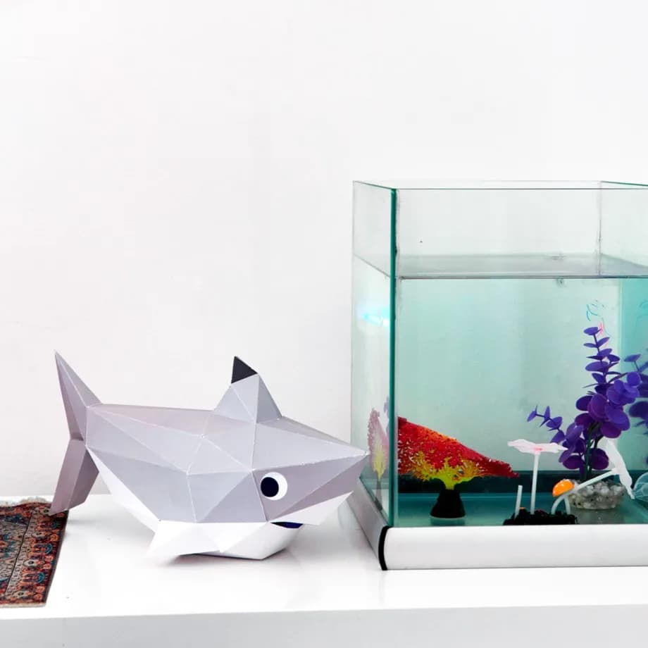 Décoration en papier trophée babies requin gris posé sur une table près d'un aquarium de poissons